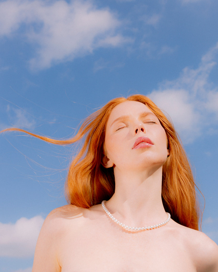A woman wearing the Classic Freshwater Pearl Necklace against a blue sky