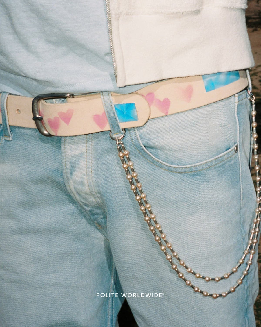 The Airbrush Belt worn over light wash jeans, pink hearts and blue gemstones painted along the leather, a silver chain at the hip