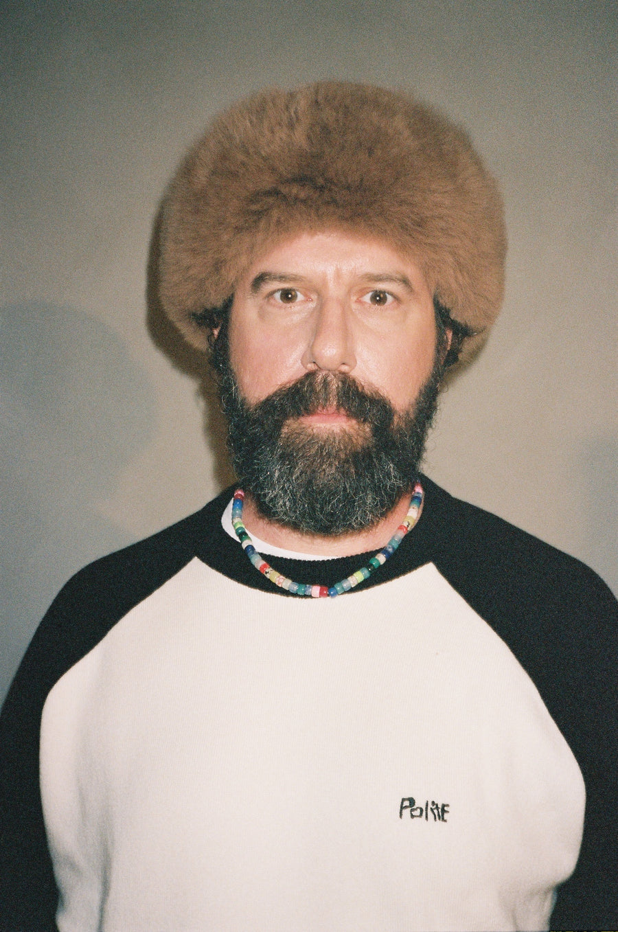 A man wearing the Cashmere Raglan Sweater, a strand of colored beads at the collar