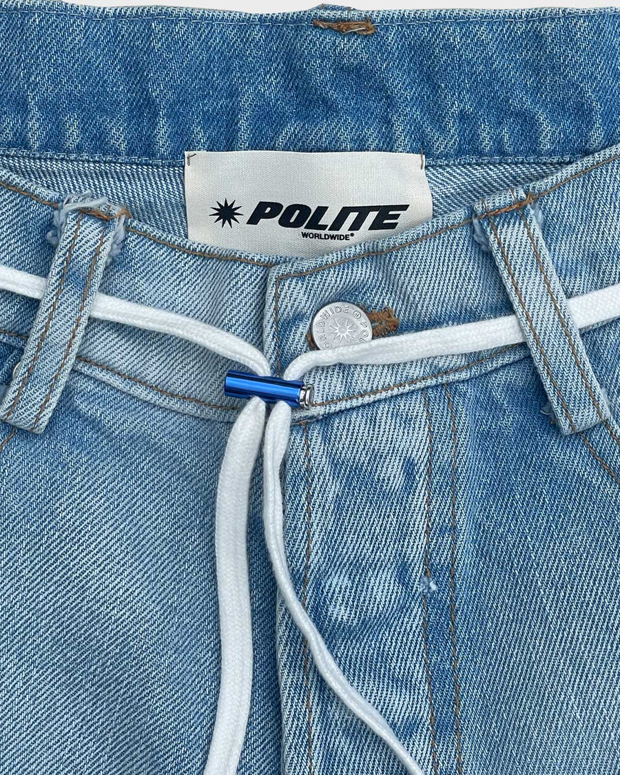 The waistband of the Deconstructed Denim Shorts: the Polite label, a brushed silver button and a white cord through the belt loops